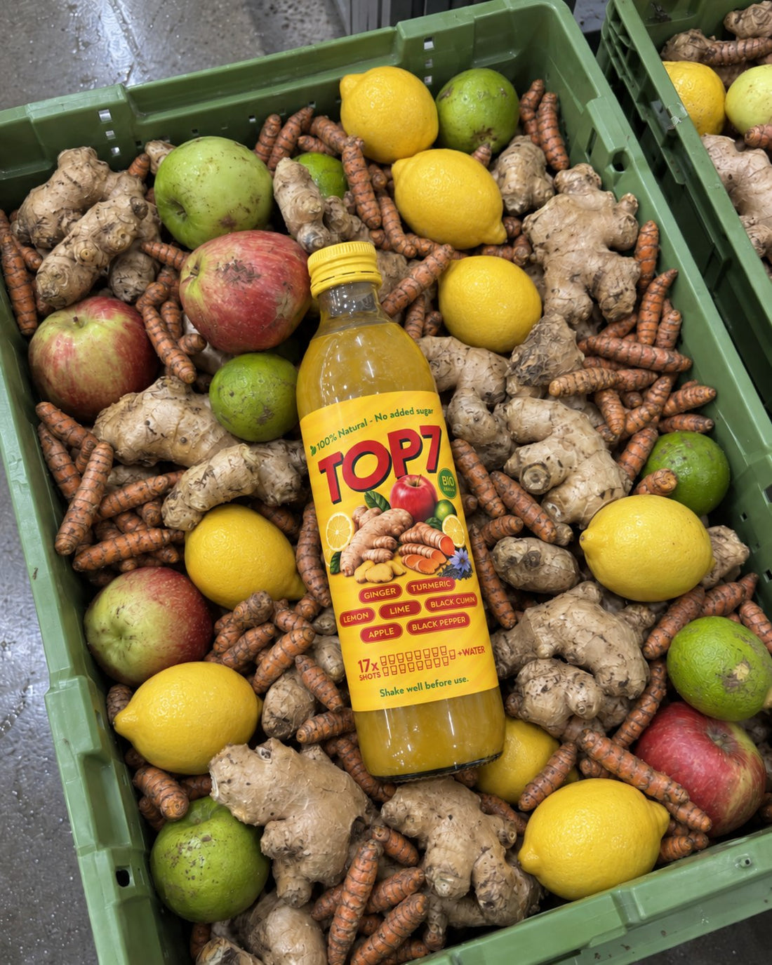 TOP 7 bottle lying on a crate of fresh ginger, turmeric, lemons, limes and apples at our production